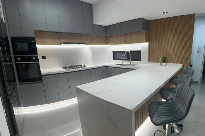 Isla de cocina en piedra clara con banquetas altas y muebles grises