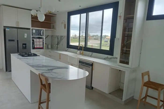 Isla de cocina en piedra clara con banquetas de madera y ventanal