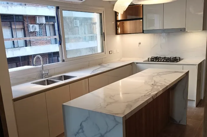 Isla de cocina con frente en piedra veteada y mesada perimetral bajo ventana