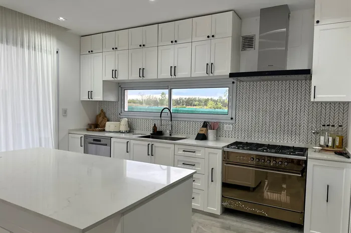 Isla de cocina en piedra clara en una cocina de frentes blancos