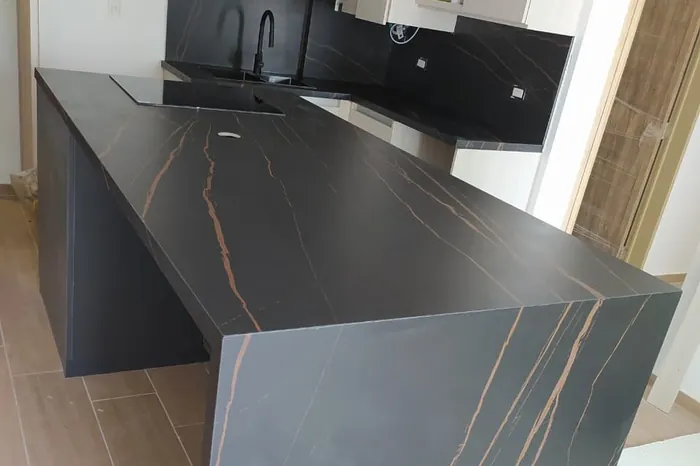 Isla de cocina en piedra negra con vetas cobrizas y caída lateral a piso