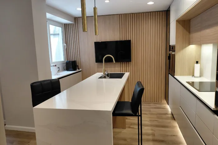 Isla de cocina larga en superficie calacatta con colgantes de bronce y frente de listones