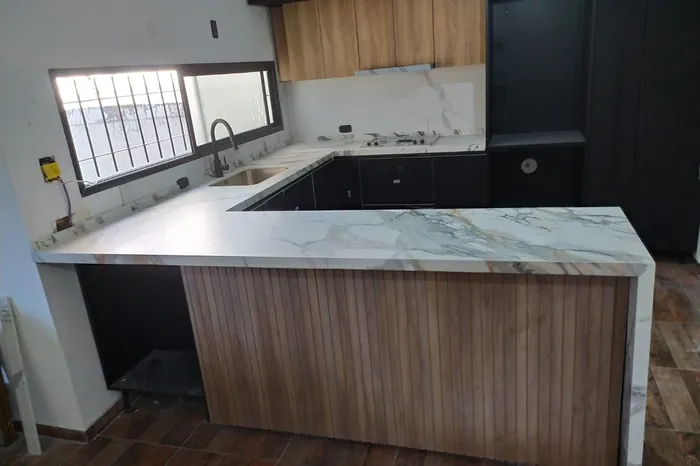 Península de cocina en mármol veteado con frente de madera y ventana